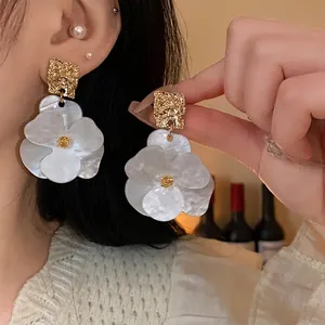 Elegant oversized white flower earrings with gold textured rectangle stud details.