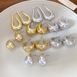 Colección de pendientes geométricos gruesos dorados y plateados en un plato blanco cerámico.