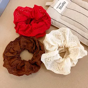 Close-up detail of three elegant eyelet lace scrunchies in red, brown and off-white