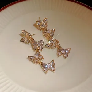 Elegant gold-tone butterfly tassel earrings with sparkling zircon crystals on white plate.