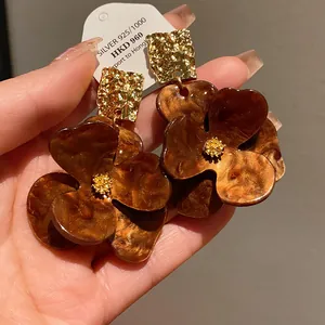 Close-up of exaggerated brown marbled floral earrings with gold hammered metal tops
