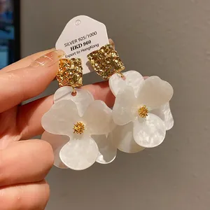 Close-up detail of oversized white flower earrings with gold textured square accents