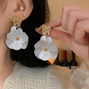 Detailed close-up of elegant white flower drop earrings with textured golden geometric studs