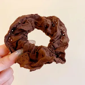 Detailed view of a brown hollow lace scrunchie with elegant pleated fabric texture.
