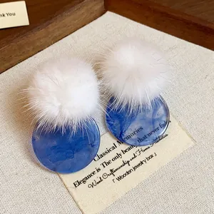 Close-up of elegant white fur pom-pom and blue marbled resin round stud earrings