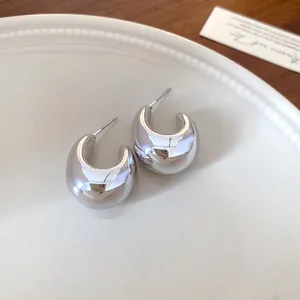 Vista detallada de pendientes de aro plateados en forma de C en plato blanco