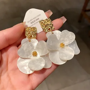Close-up of white pearlescent flower earrings with a textured gold square stud
