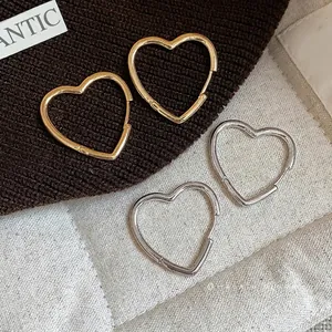 Minimalist gold and silver heart-shaped polished hoop earrings on textured fabric