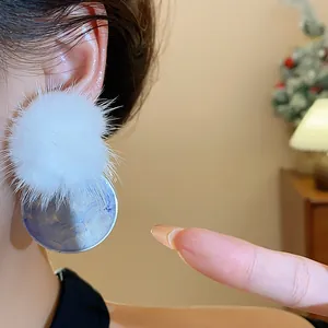 Close-up of elegant white fur pom-pom and blue marble resin stud earring on model's ear