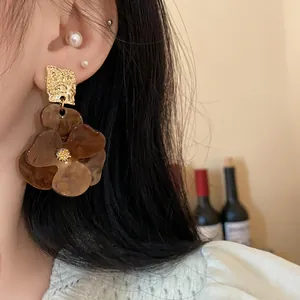 Close-up of exaggerated flower earrings with amber brown petals and golden hammered stud.