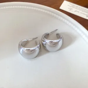 Vista detallada de pendientes de aro plateados en forma de U sobre un plato de cerámica