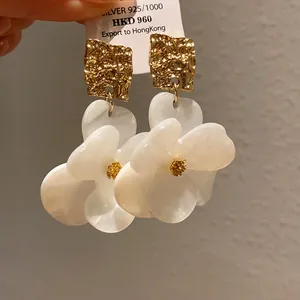 Detailed close-up of white resin flower earrings with textured gold studs and silver 925 tag.