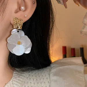Close-up detail of white pearlescent flower earrings with golden textured metal studs