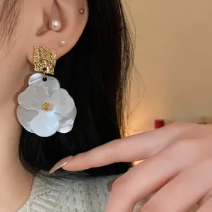 Detailed view of an oversized pearlescent flower earring with gold textured stud