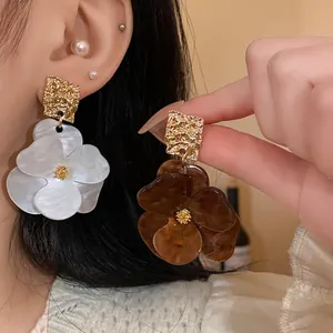Detailed view of oversized acrylic flower earrings with golden textured geometric studs.