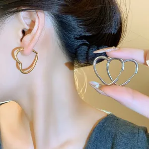 Close-up of minimalist gold and silver heart-shaped hoop earrings on model