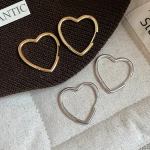Minimalist gold and silver heart-shaped hoop earrings on textured fabric background