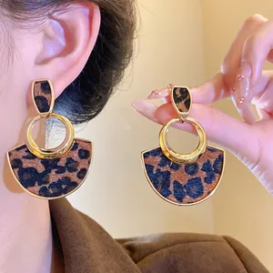 Close-up detail of stylish leopard print hollow earrings with gold trim on an Asian model