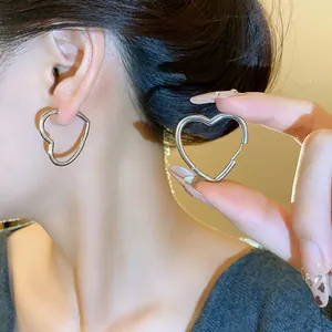 Close-up of minimalist heart-shaped silver hoop earrings worn on ear and held by hand