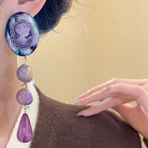 Close-up of vintage cameo drop earrings with purple resin beads and iridescent finish