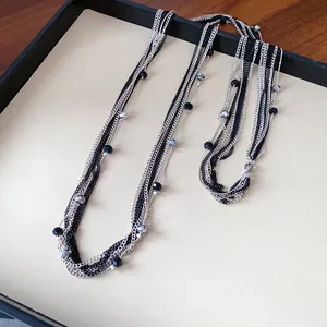 Dettaglio di un'elegante collana a più strati con catene e perle di vetro nere e argento.