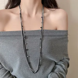 Dettaglio di una collana a strati con perle di vetro nere e catenine d'argento sul collo
