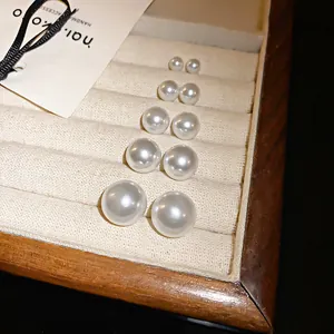 Primer plano de pendientes de perlas de varios tamaños en una bandeja de joyería beige.