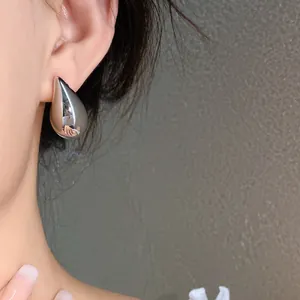 Primer plano de un pendiente de botón minimalista de gota de plata en el lóbulo de la oreja