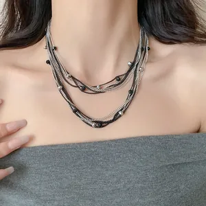 Dettaglio di un'elegante collana multistrato con perle di vetro nere e argento in primo piano.