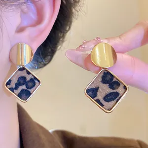 Close-up of leopard print square drop earrings with elegant gold circular studs