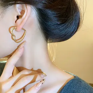 Detailed close-up shot of minimalist heart-shaped gold hoop earrings worn on a model ear