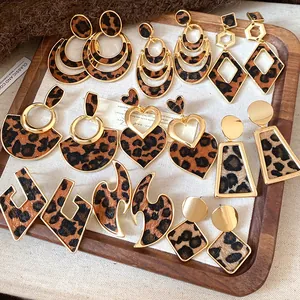 Variety of leopard print geometric earrings in gold-toned settings on a wooden tray