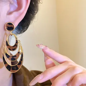 Detailed view of layered oval leopard print earrings with gold-tone frames on model