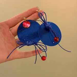 Close-up view of blue circular drop earrings with red bead and blue knot details