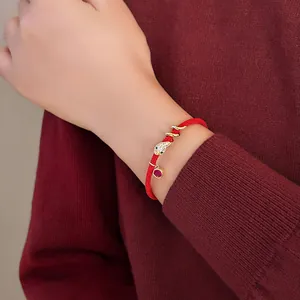Nahaufnahme eines eleganten roten Schnurarmbands mit vergoldetem Schlangenanhänger am Handgelenk.