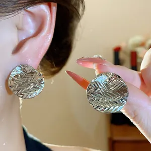 Close-up detail of silver pleated round stud earrings featuring a textured chevron pattern