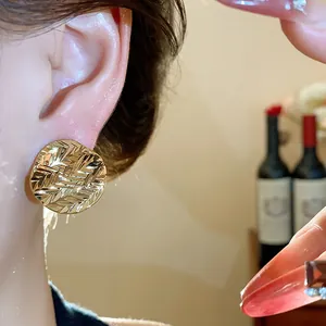 Detailed view of luxury 18k gold-plated pleated round stud earrings on model's ear