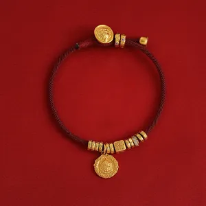Nahaufnahme eines vergoldeten roten Seilarmbands mit filigranem Gottheitsanhänger