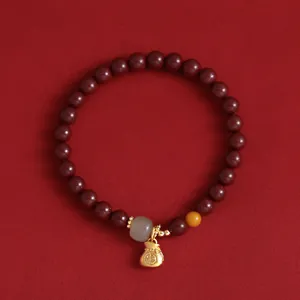 Rotes Perlenarmband mit goldenem Geldbeutel-Anhänger und chinesischem Glückssymbol.