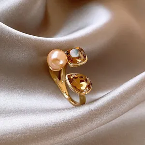 Detailaufnahme eines vergoldeten offenen Rings mit Perle und bernsteinfarbenen Kristallen