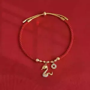 Detailaufnahme eines vergoldeten Schlangenanhängers mit Zirkonia-Inlay an einem roten Seilarmband