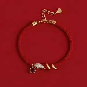 Detailansicht eines vergoldeten Schlangen-Armbands aus roter Kordel mit Zirkonia