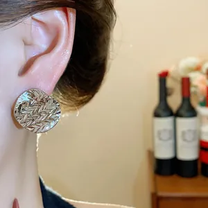 Close-up of silver textured round stud earring on ear with wrinkled design.