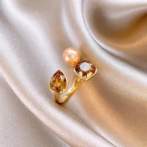 Makroaufnahme eines vergoldeten offenen Rings mit Perle und bernsteinfarbenen Kristallen.