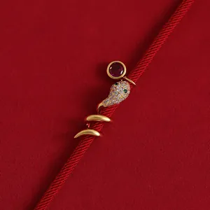 Nahaufnahme eines vergoldeten Schlangen-Charms mit Zirkonia auf einem roten Band
