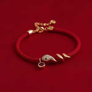 Nahaufnahme eines vergoldeten Schlangenarmbands aus roter Kordel mit Zirkonia