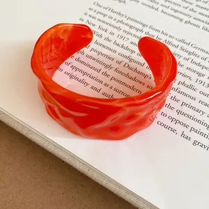 Primo piano di un bracciale rigido retrò in acrilico arancione con trama ondulata unica