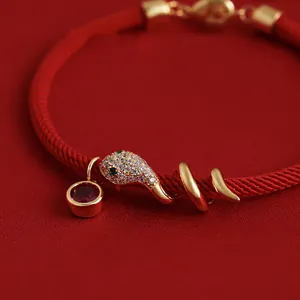 Nahaufnahme des vergoldeten Schlangenanhängers mit Zirkonia auf einem roten Stoffarmband.