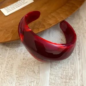 Primo piano di un bracciale rigido vintage in acrilico rosso traslucido su vassoio.