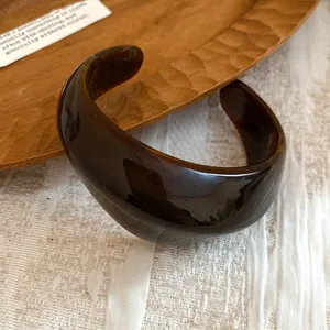 Dettaglio macro di un bracciale rigido aperto in acrilico ambrato lucido stile retrò